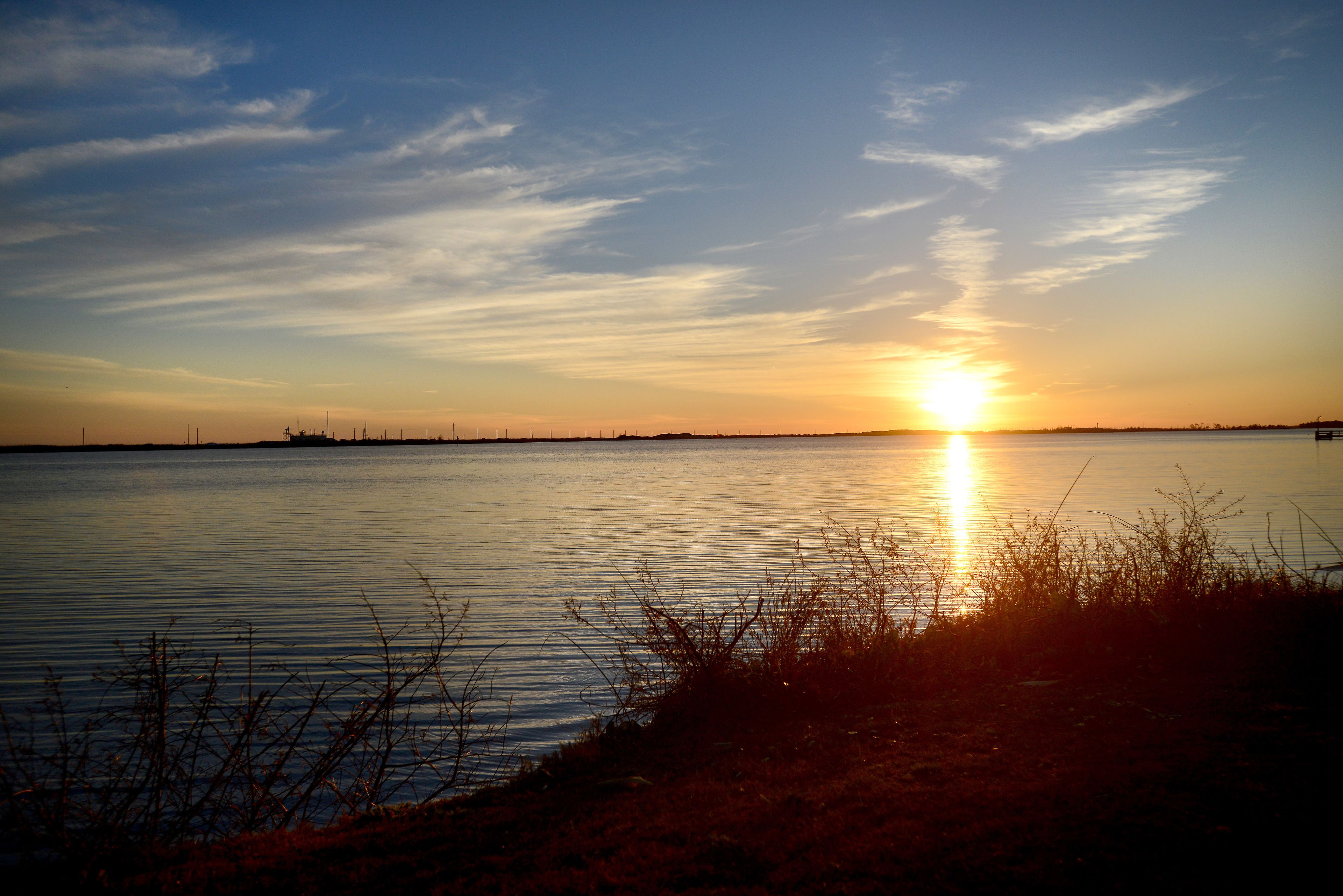A sunset over a calm body of water with distant land visible on the horizon.