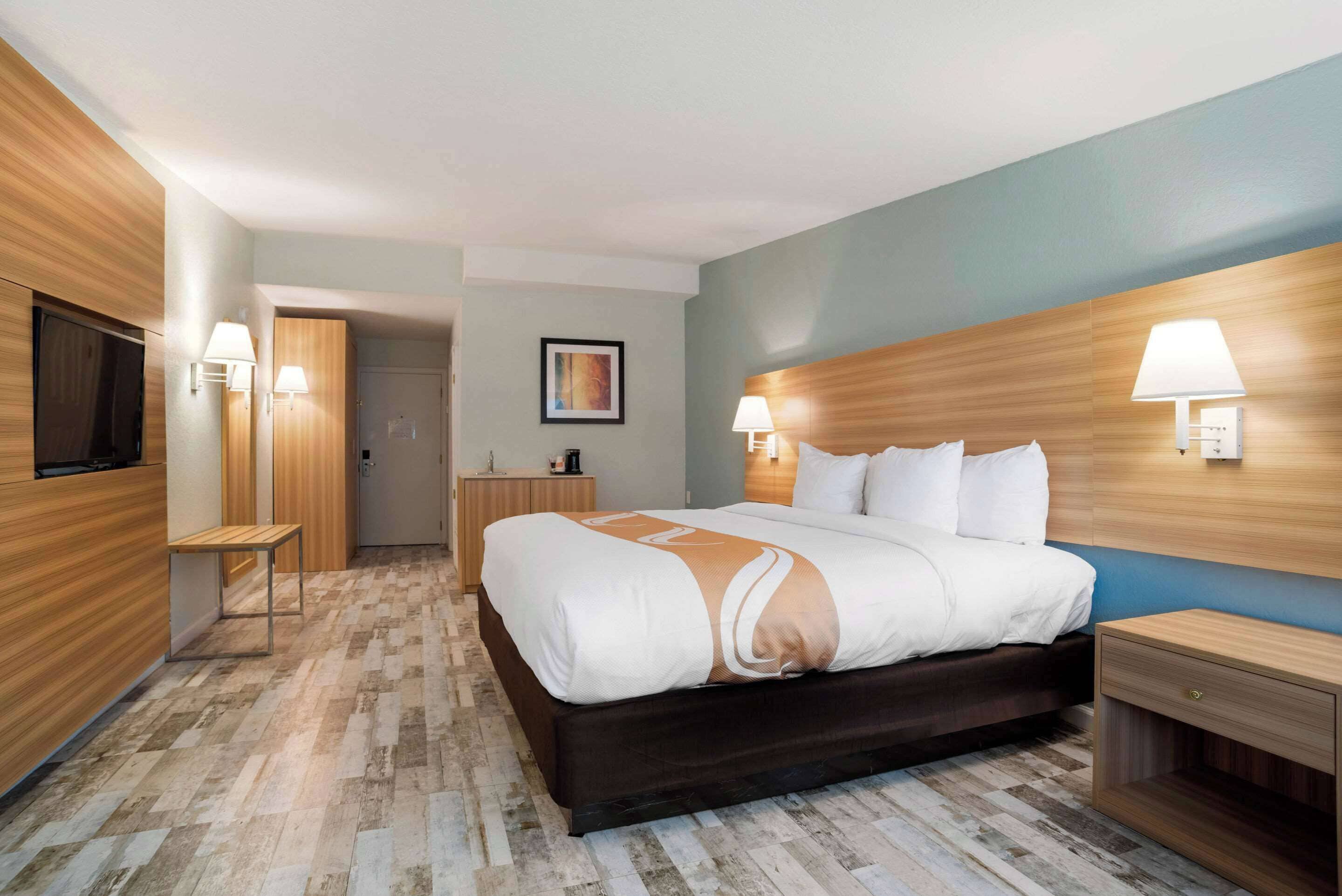Une chambre d’hôtel avec un grand lit, une tête de lit en bois, des lampes de chevet, une petite table et un téléviseur.