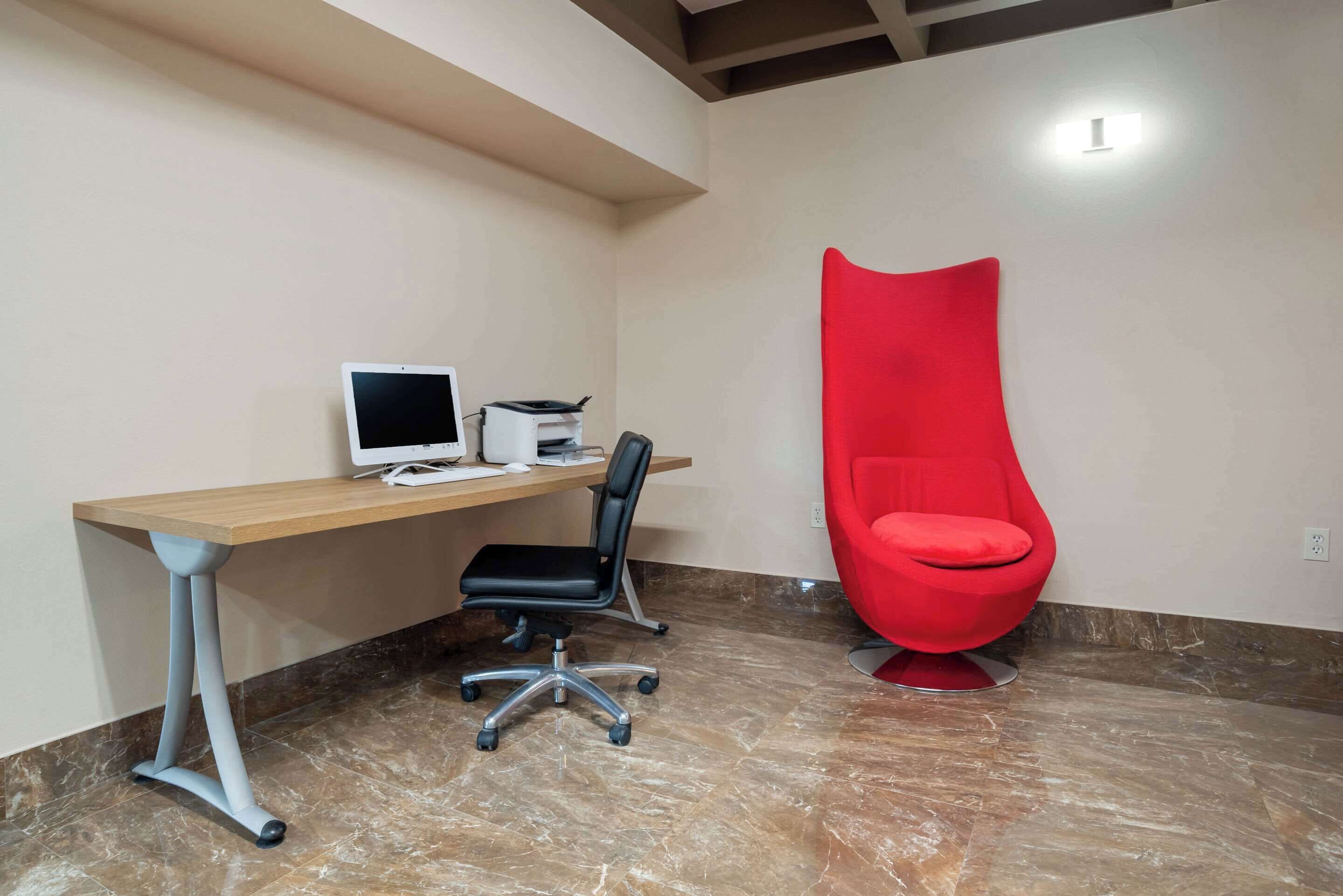 A modern office with a desk, computer, and a red chair.