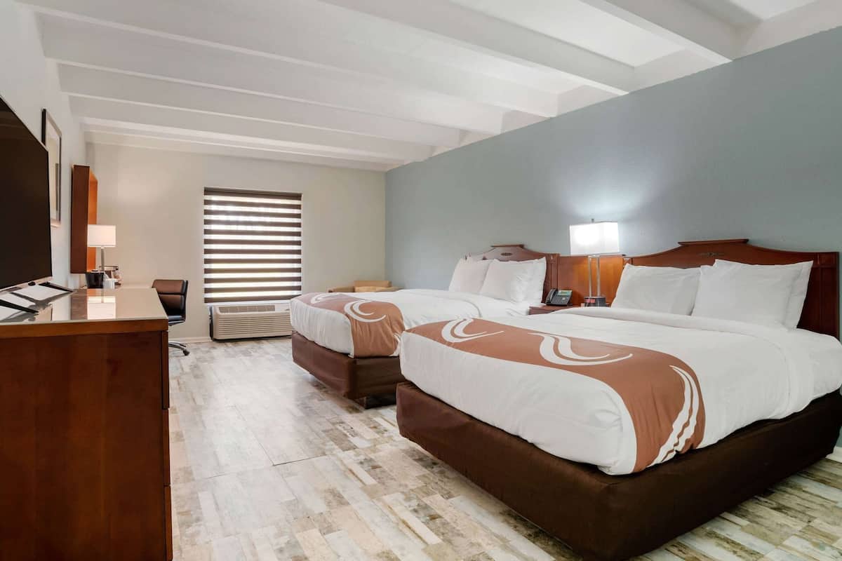 Quarto de hotel com uma cama grande, duas mesas de cabeceira, uma escrivaninha e uma cadeira.