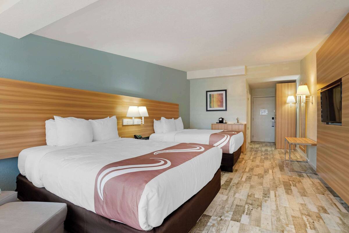 Quarto de hotel com uma cama grande, mesa de cabeceira, abajur e televisão.