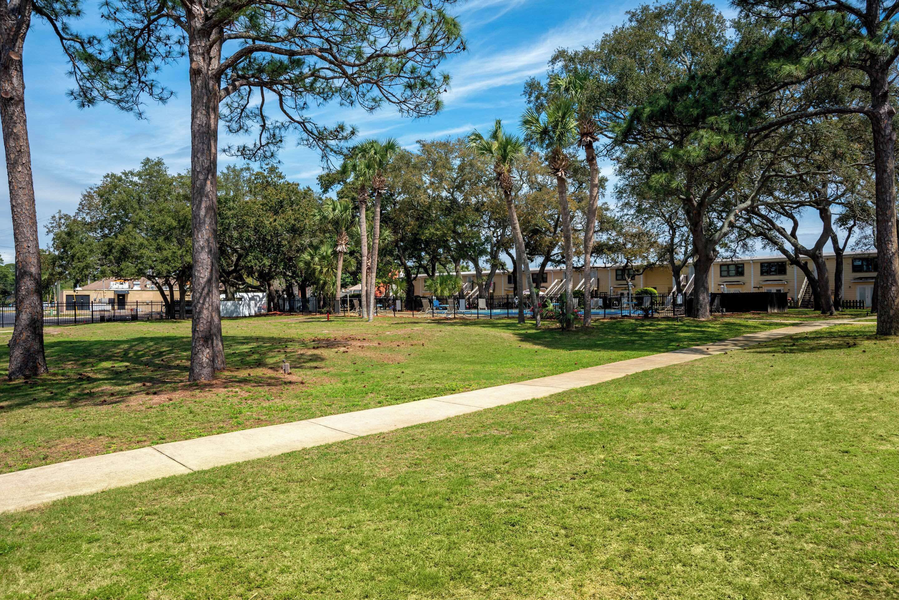 A park with a paved walkway, trees, and a building in the background.