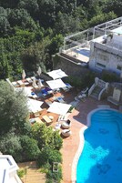 An outdoor swimming pool area with lounge chairs and umbrellas, surrounded by greenery.