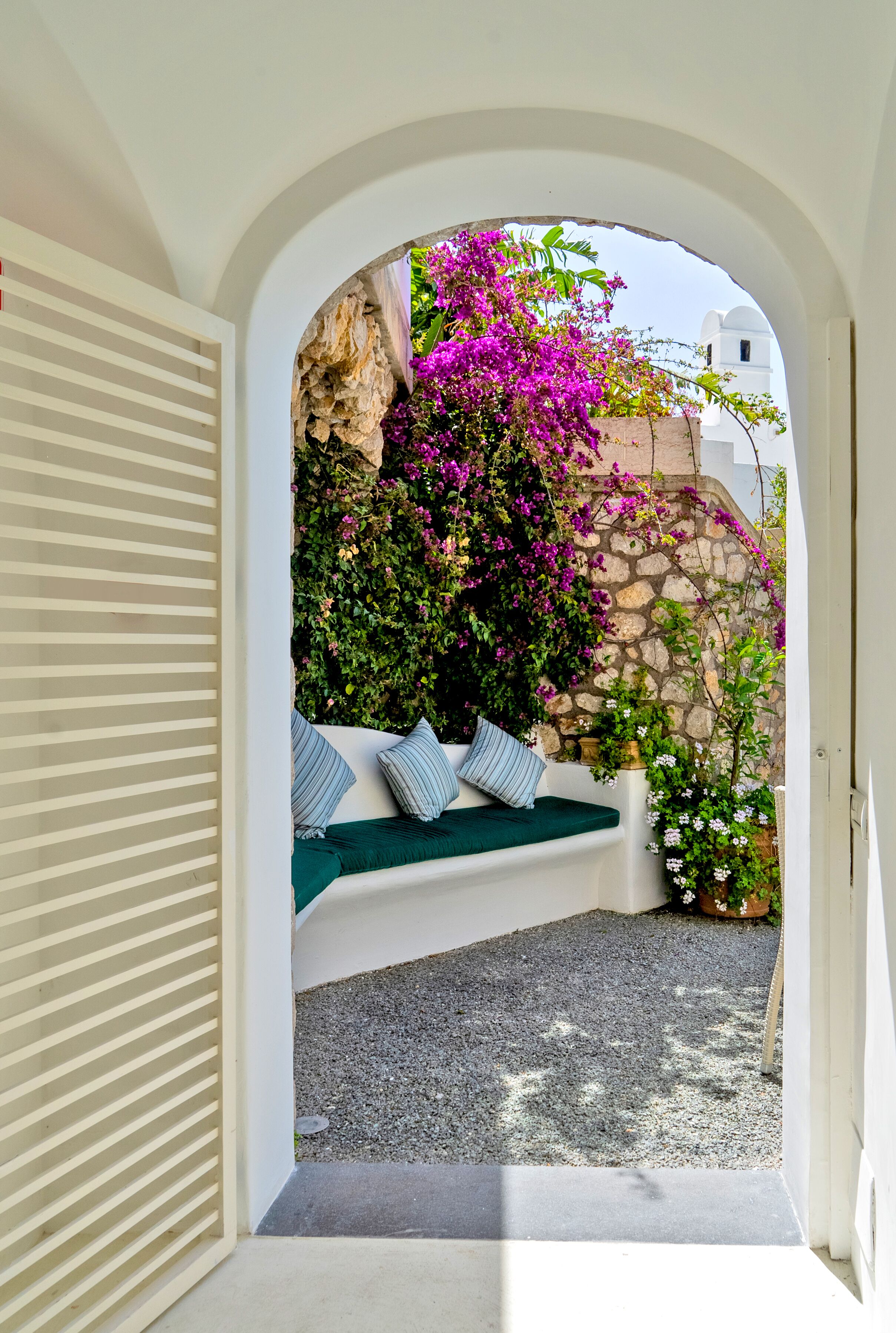 Un arco de entrada da a una zona de estar con pared de piedra y plantas florecientes.