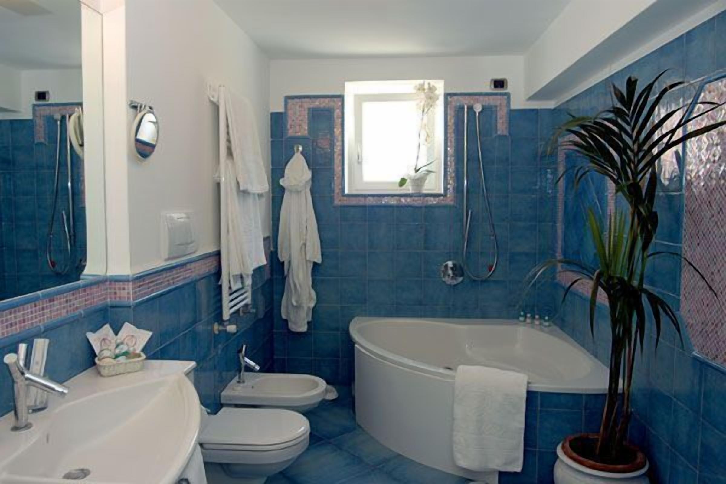 Un baño con bañera, lavabo e inodoro. Se ve una ventana con una planta en el alféizar.