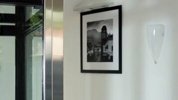Ein Flur mit einem in Schwarzweiß gerahmten Foto an der Wand, einer Leuchte und einer Glastür zu einem Aufzug.