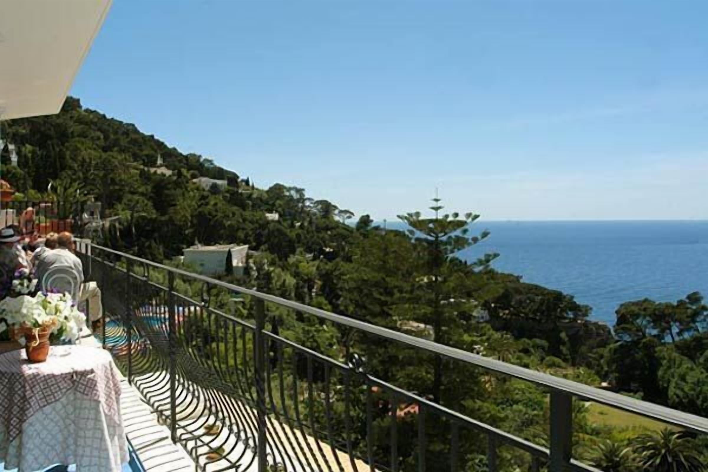 A balcony with a view of the sea, surrounded by greenery.