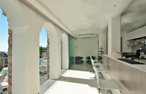 A modern outdoor bar area with a pool view, white bar stools, and a stone wall.