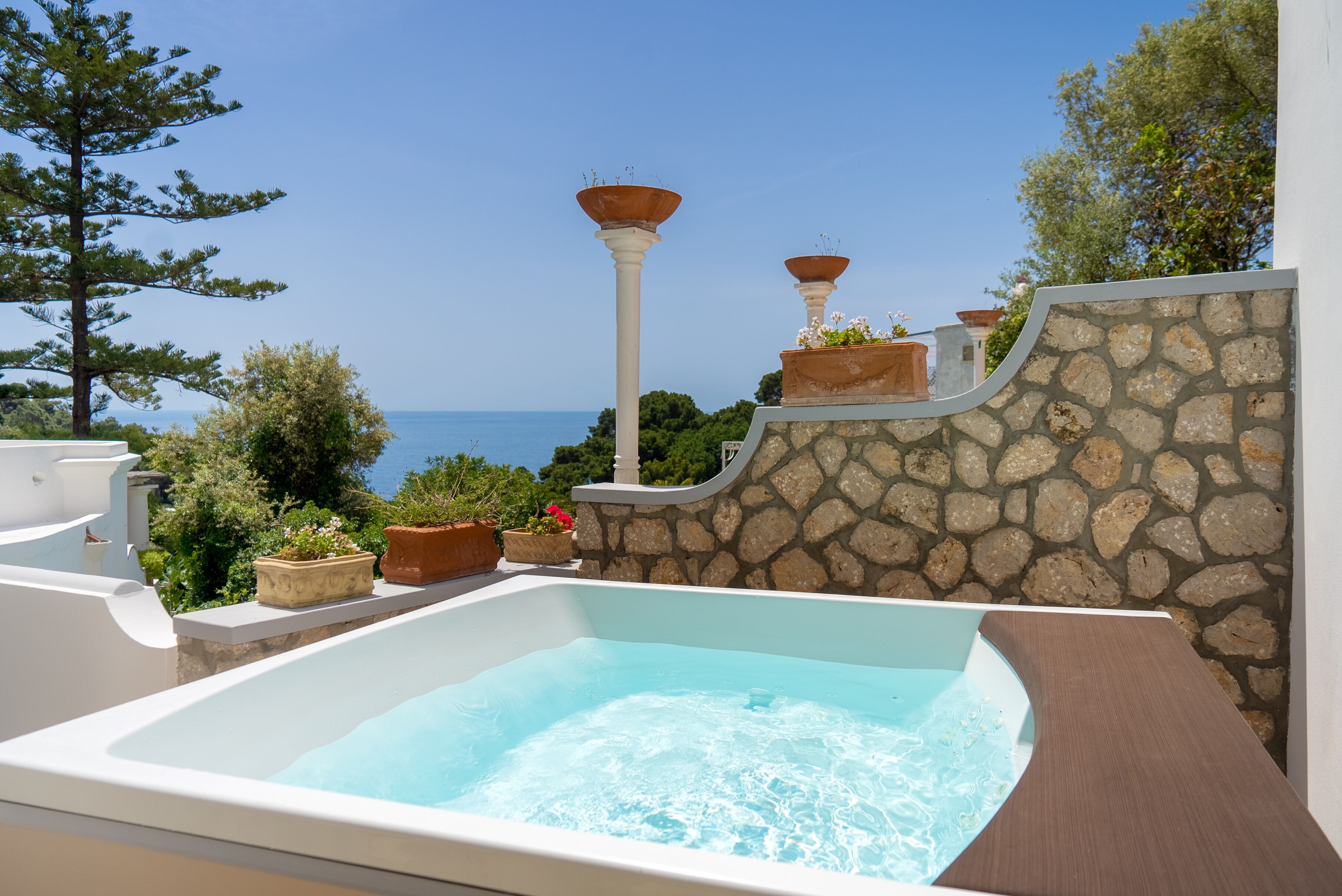 A hot tub with a stone wall backdrop, overlooking a scenic view of the sea.