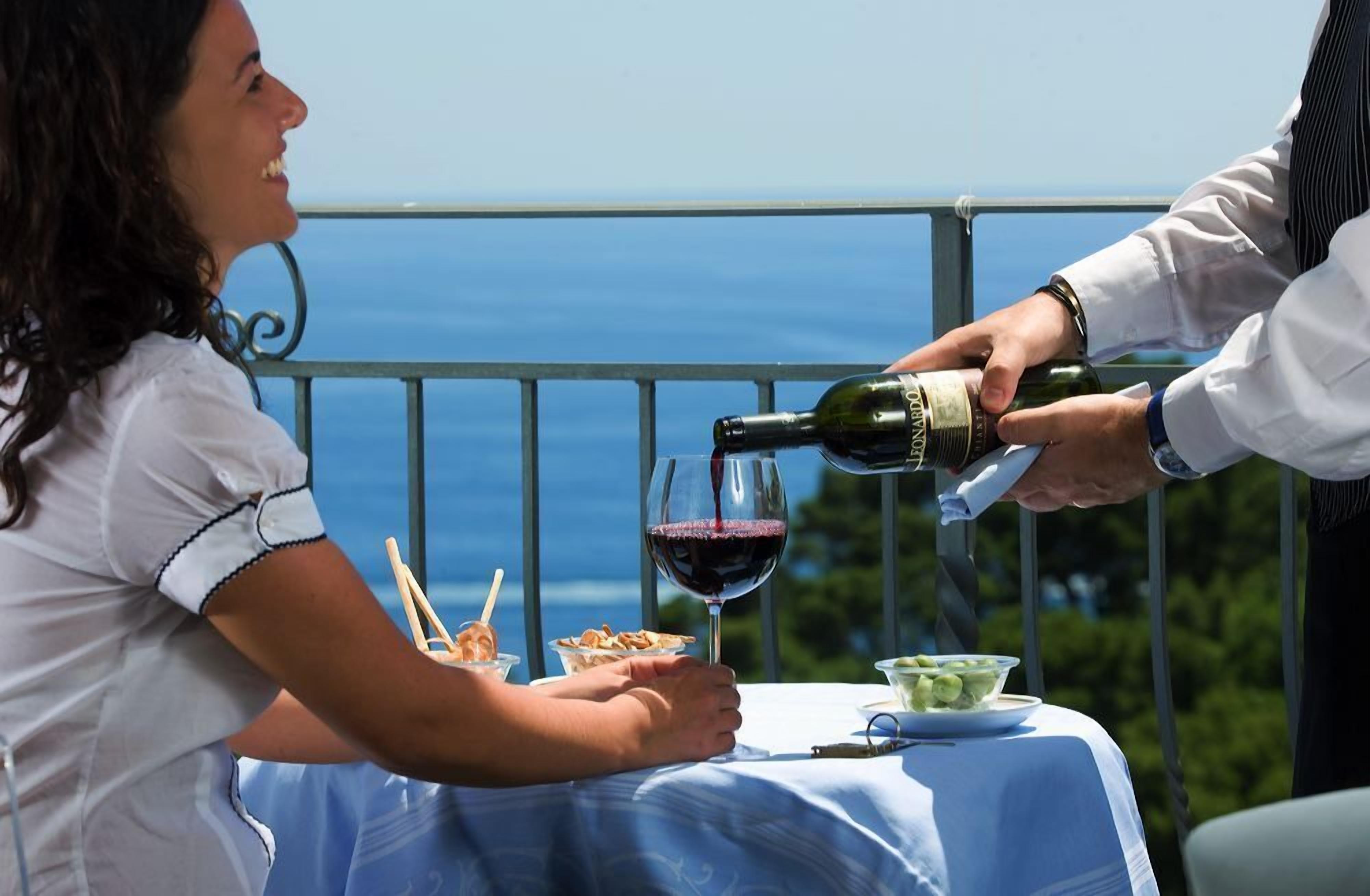 A person pouring wine into a glass at a table with a view of the sea.