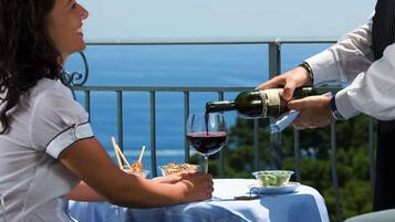 A person pouring wine into a glass at a table with a view of the sea.