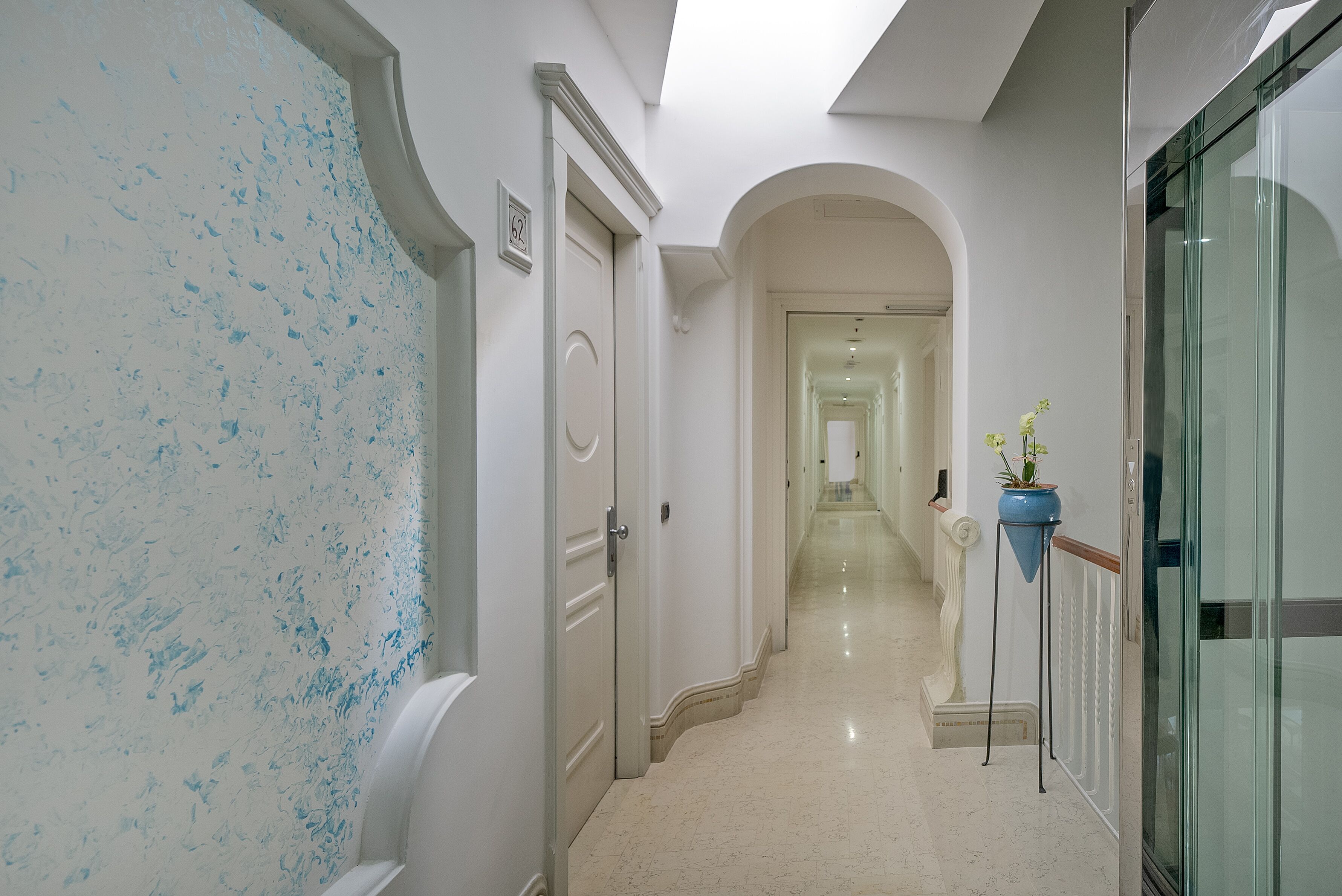 A hallway with white walls, a marble floor, and a glass door on the right.