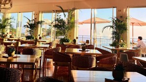 Un restaurante con terraza, grandes ventanales y plantas en macetas.
