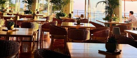 A restaurant with outdoor seating, large windows, and potted plants.