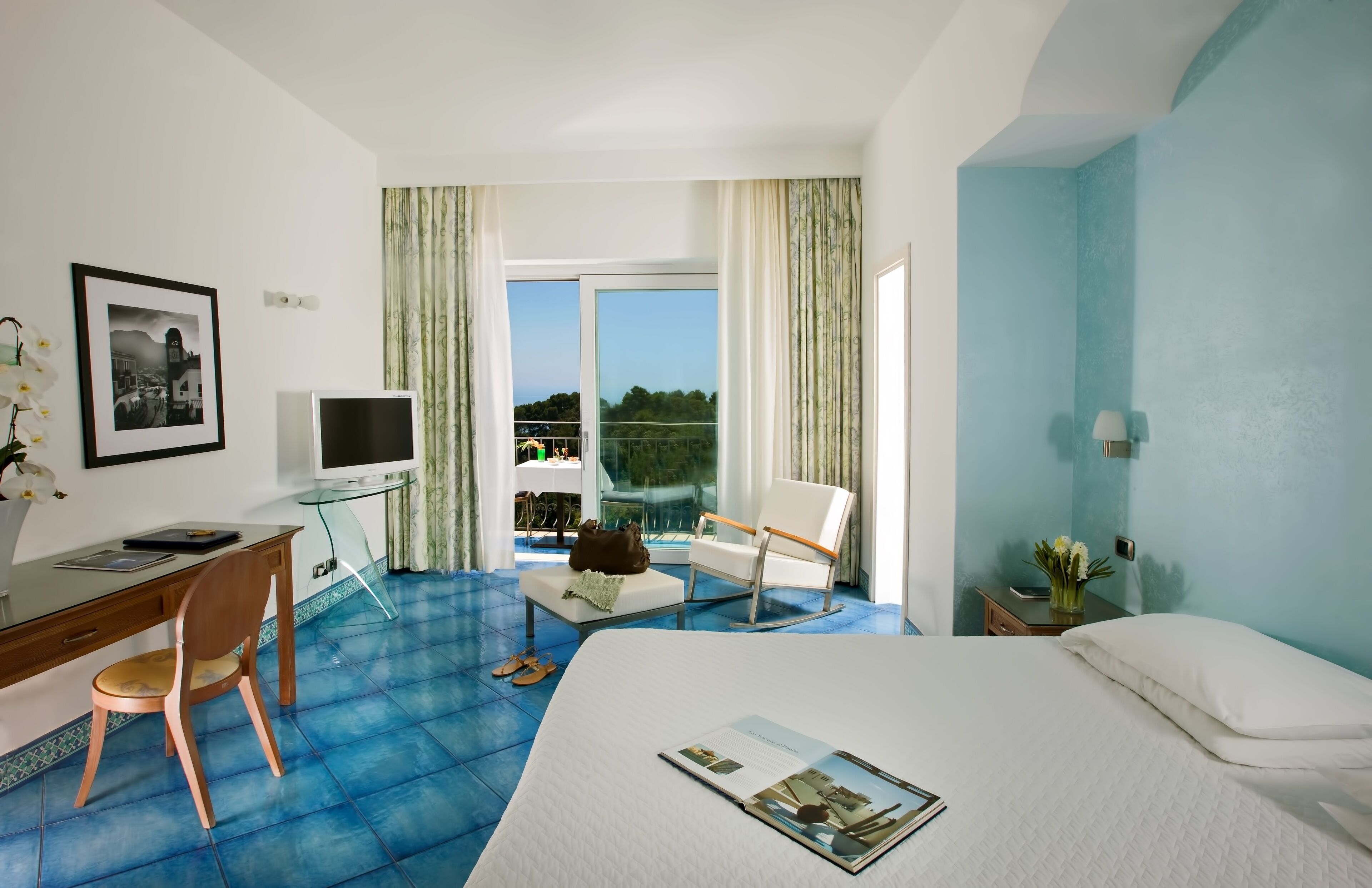 Ein Hotelzimmer mit Bett, Schreibtisch mit Stuhl, Fernseher und einem Balkon mit Blick.