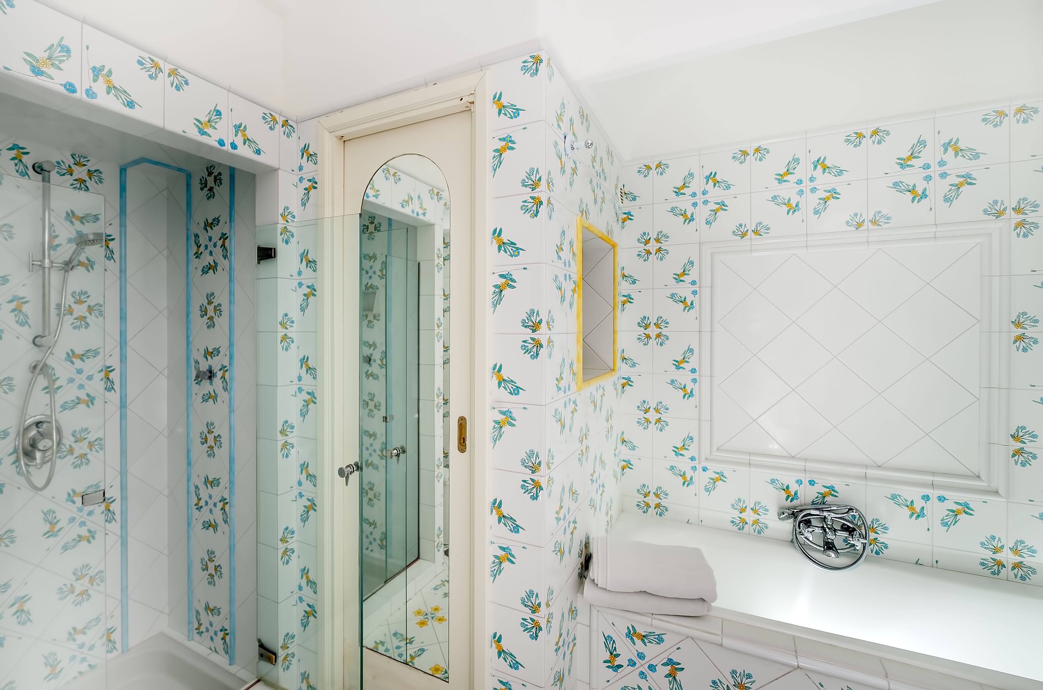 A bathroom with floral tile patterns, a glass shower enclosure, and a white sink with a chrome faucet.