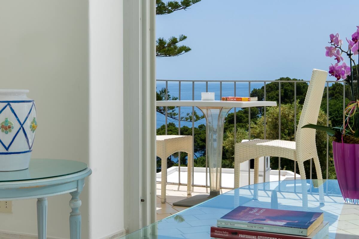 A balcony with a glass table, wicker chairs, and a potted orchid.