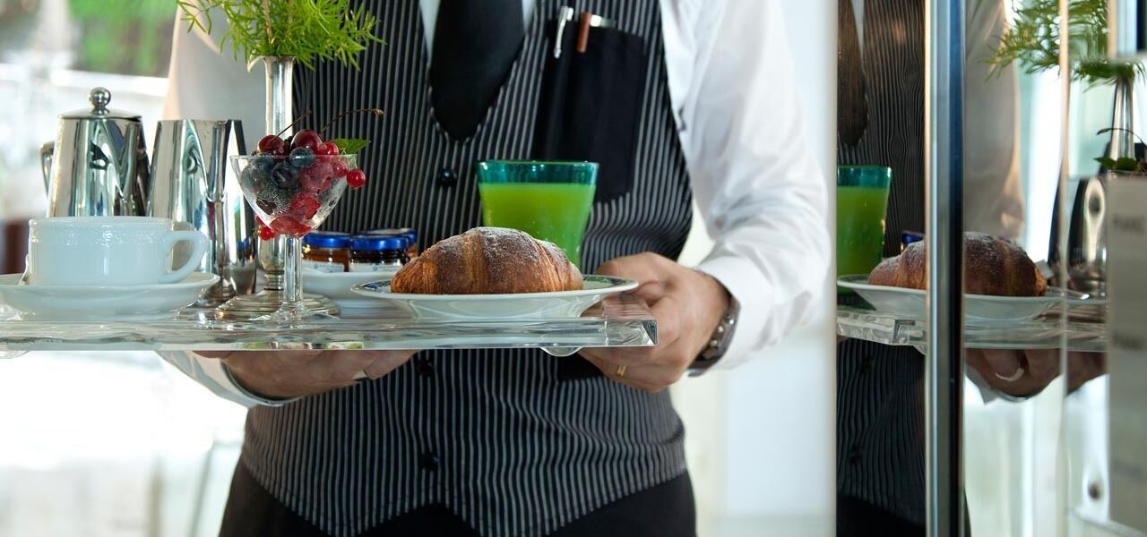 A person holding a tray with a croissant, a glass of green juice, and a bowl of berries.