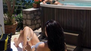 Zona de piscina con jacuzzi, sillones reclinables y plantas en macetas.