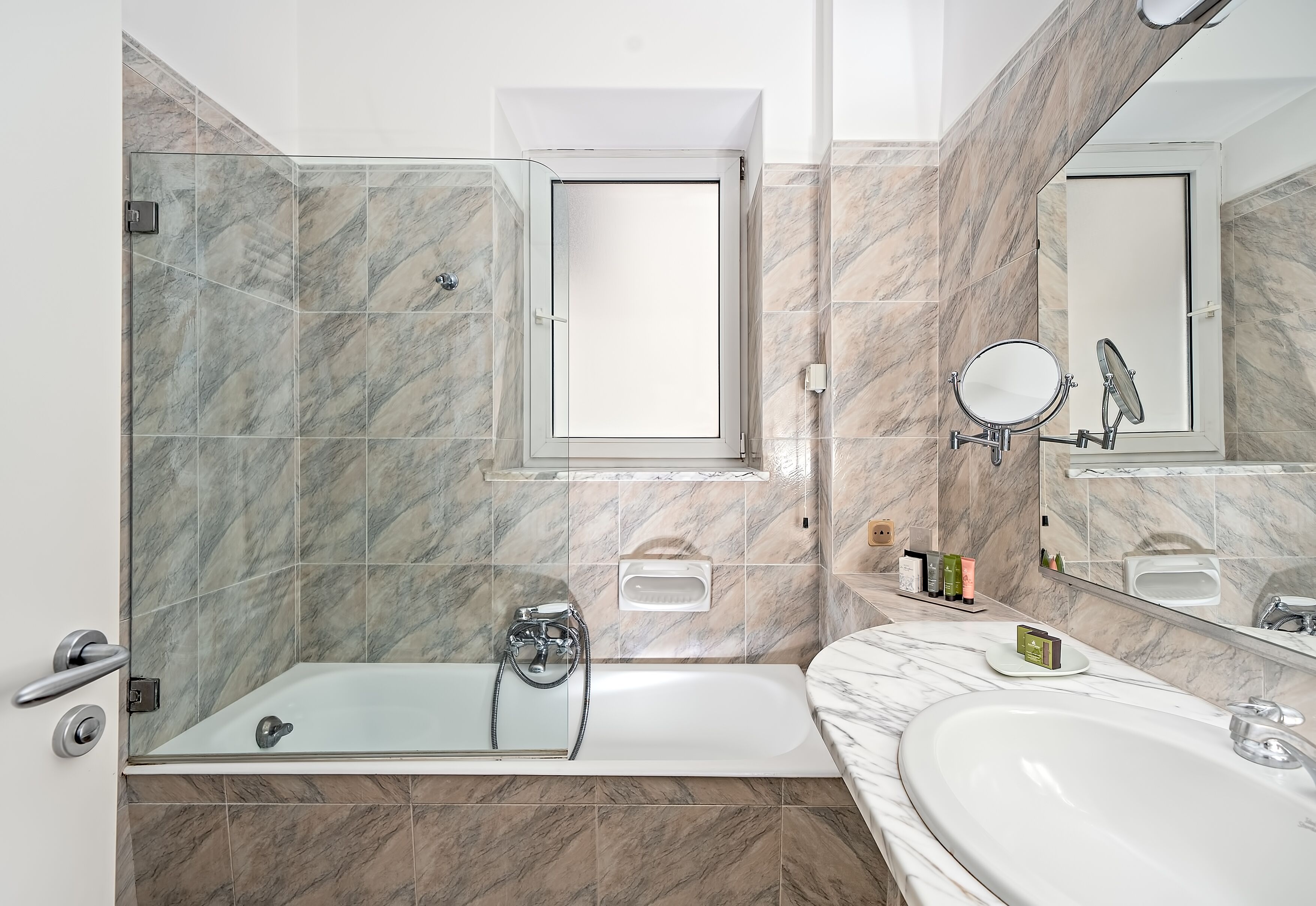 Un bagno moderno con doccia vetrata, uno specchio grande e una parete rivestita in marmo.
