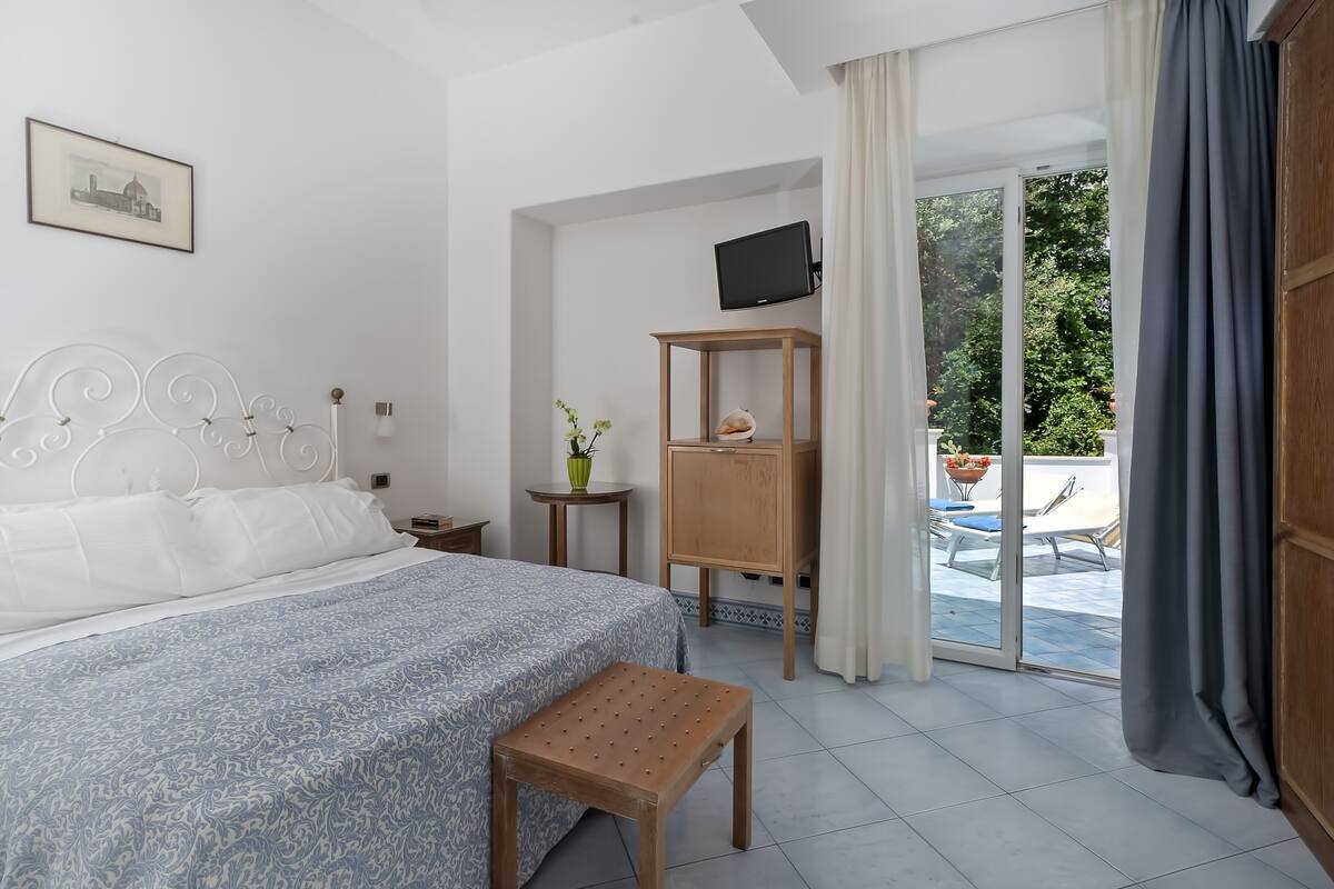 A bedroom with a bed, a small table with a vase, a wooden cabinet, and a TV on a stand.