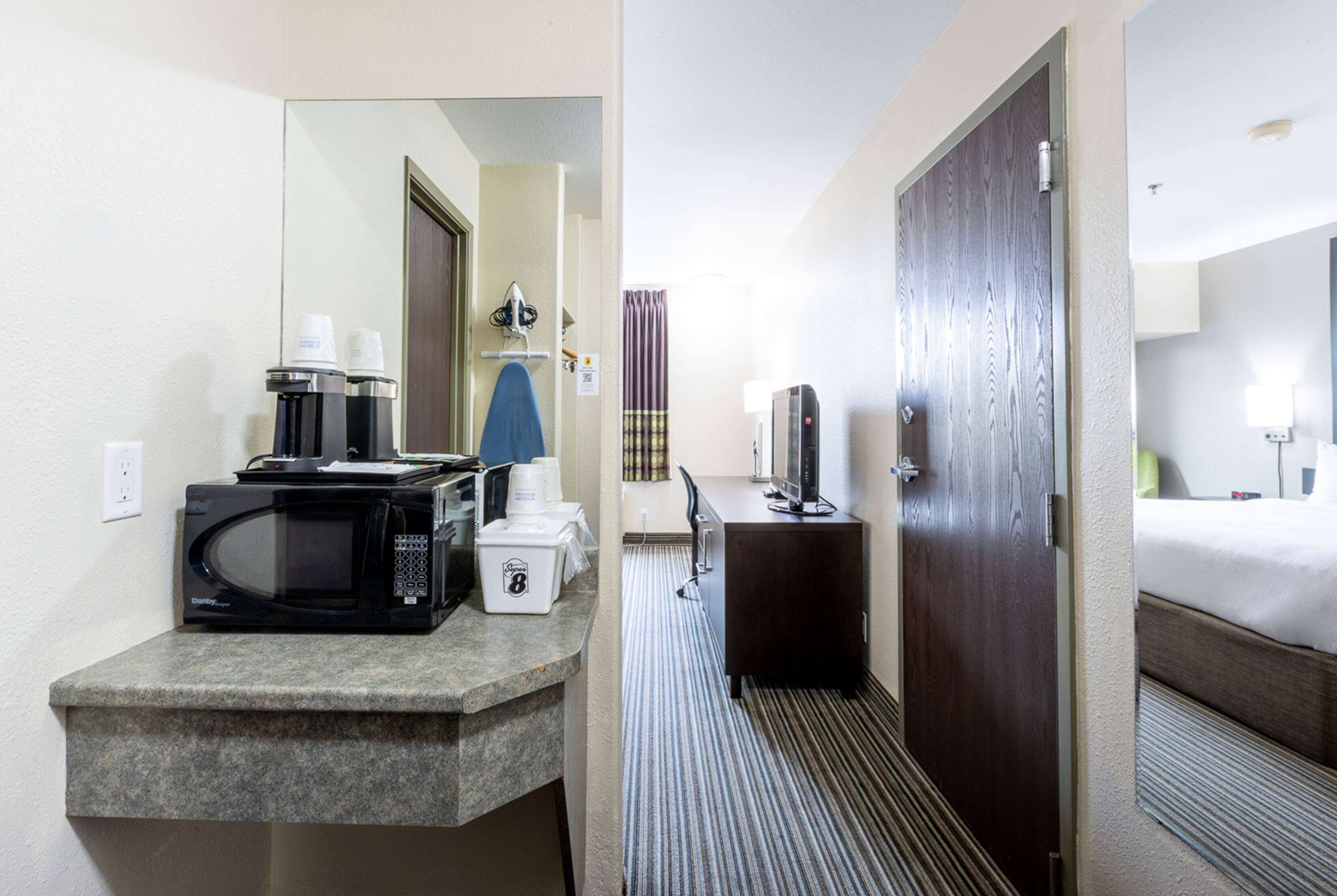A hotel room with a kitchenette, a bed, a bathroom, and a door leading to another room.
