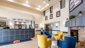 Un hall d’entrée avec un comptoir de réception, des fauteuils bleus et jaunes, une cheminée en pierre et des œuvres d’art encadrées accrochées aux murs.