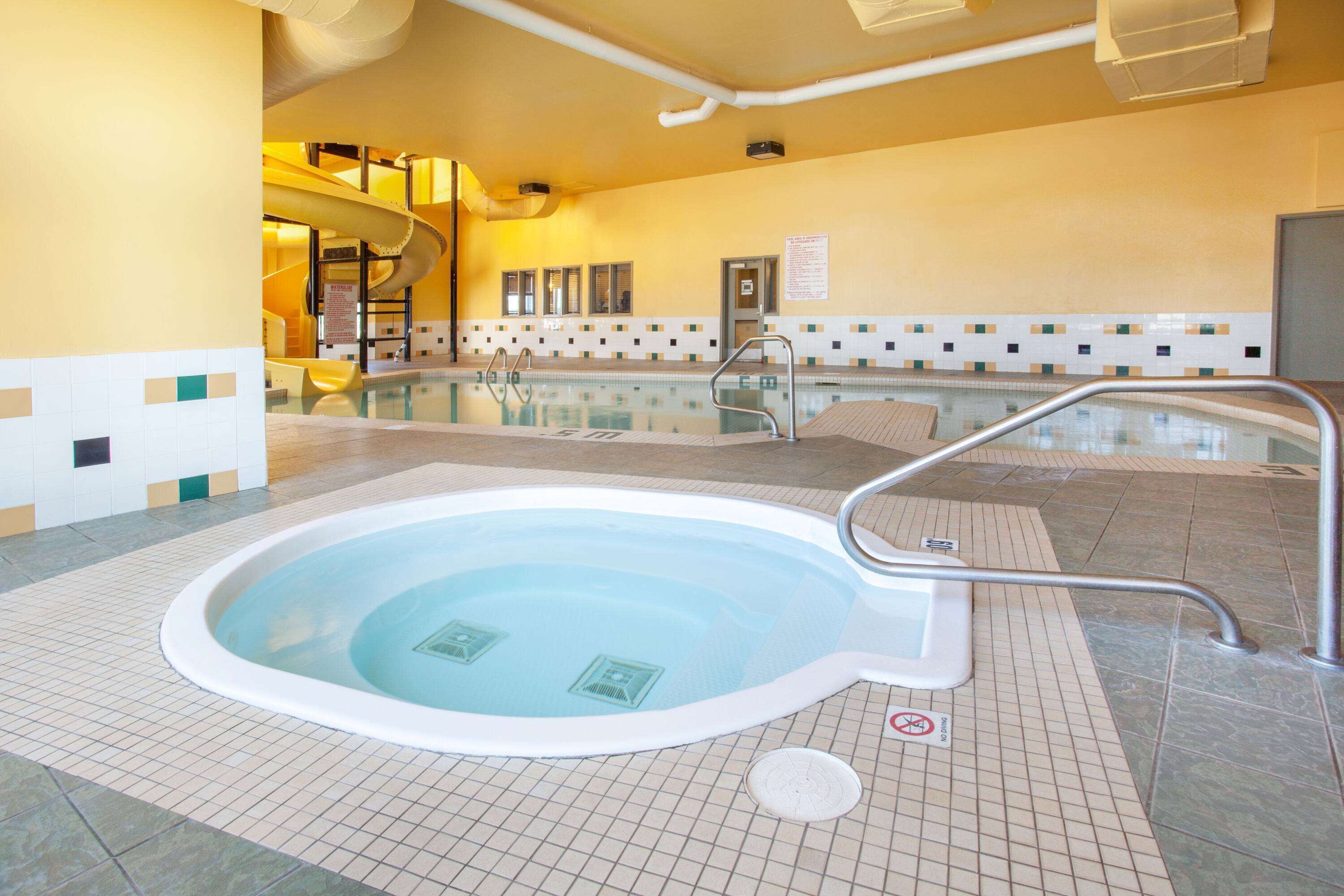 Una piscina interior con jacuzzi, suelo de baldosas y señal de prohibido bucear.