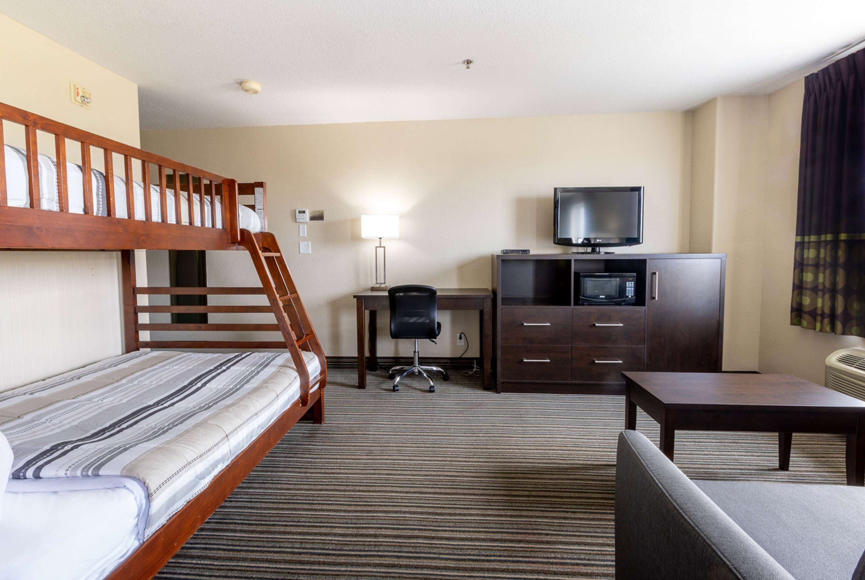 Une chambre d’hôtel avec un lit superposé, un bureau avec une chaise, une télévision, une armoire et une petite table.
