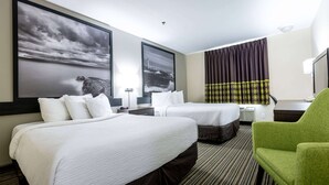 Une chambre d’hôtel avec deux lits, un fauteuil vert et des œuvres d’art accrochées aux murs.