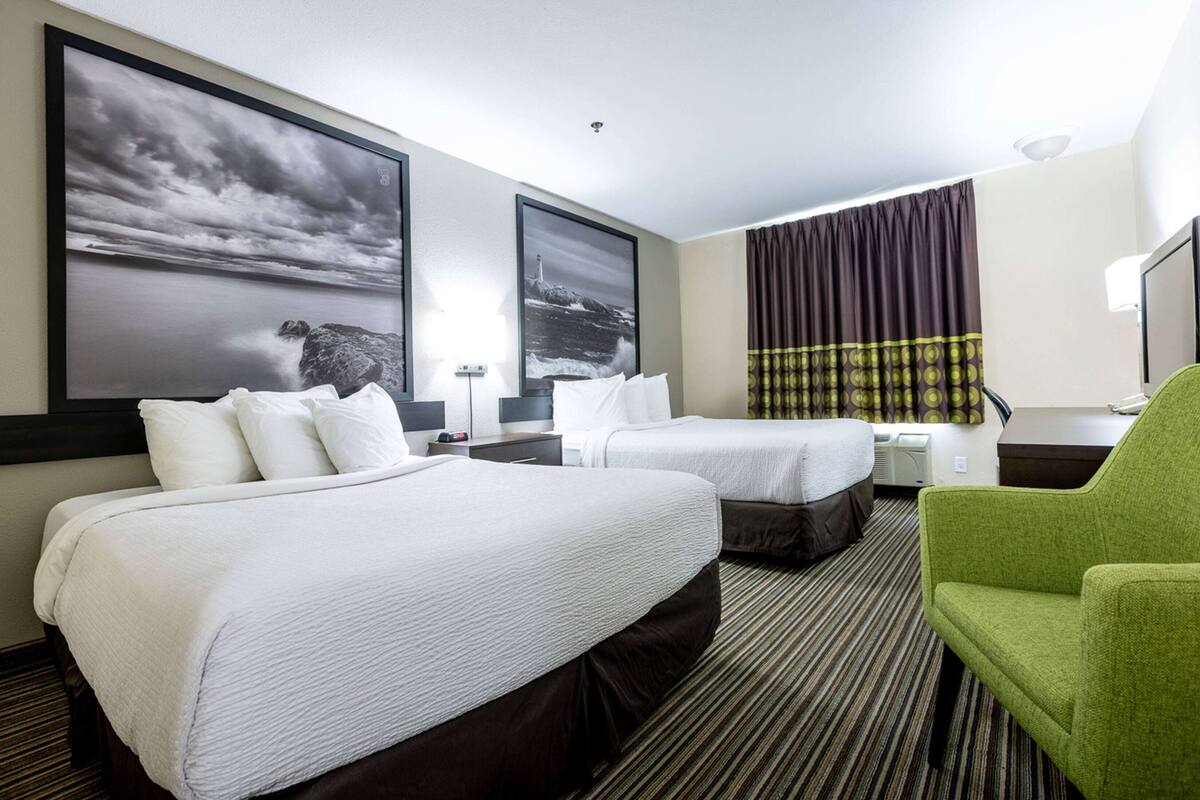 Habitación de hotel con dos camas, un sillón verde y obras de arte en las paredes.