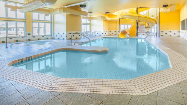 Une piscine intérieure avec un toboggan, un revêtement de sol carrelé et de grandes fenêtres.