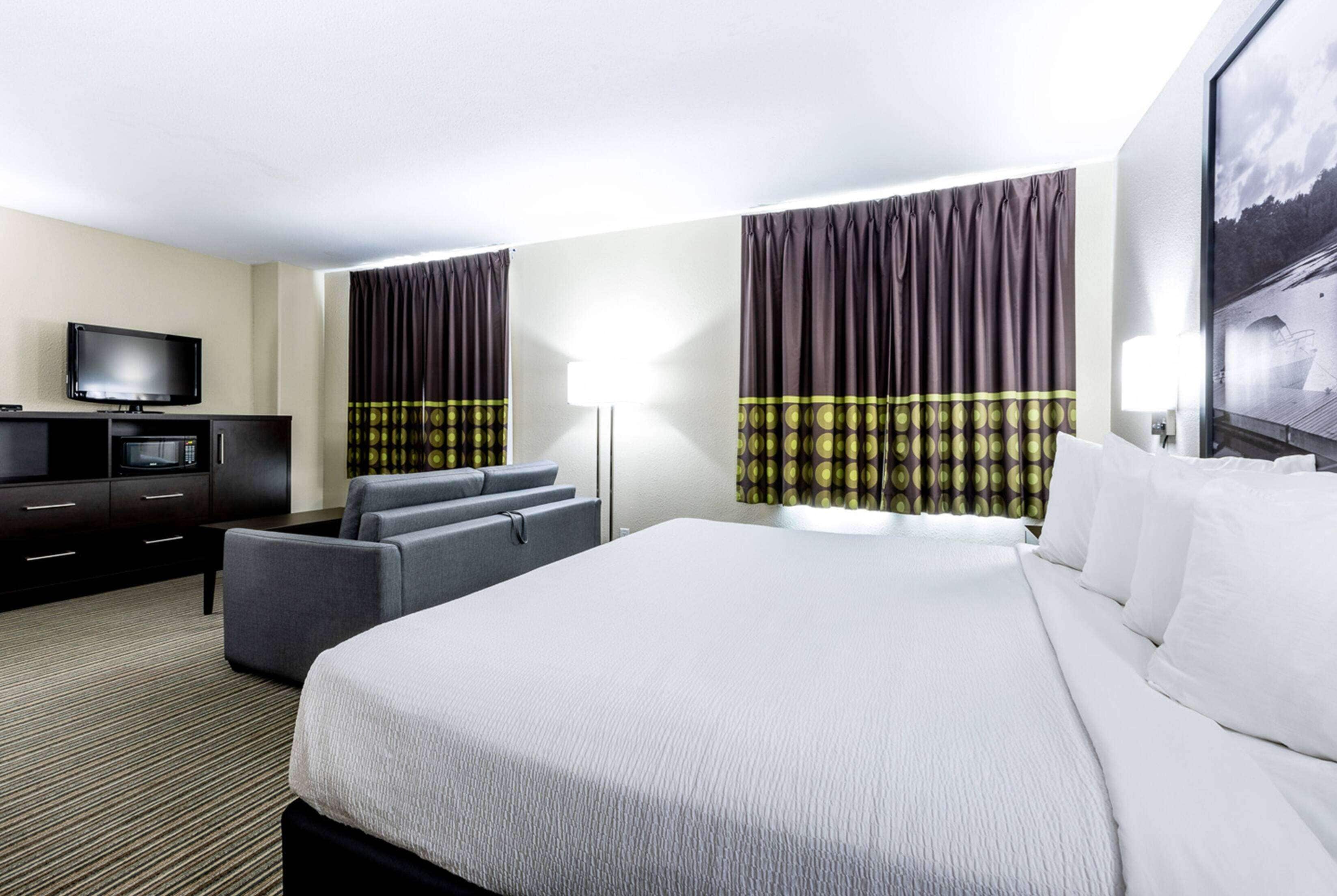 Habitación de hotel con una cama grande, un televisor de pantalla plana, un sofá y un escritorio con lámpara.
