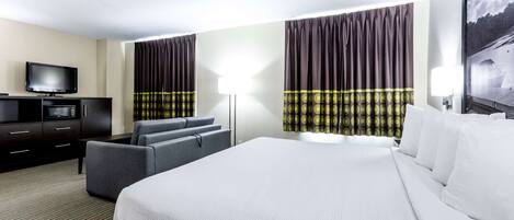 Habitación de hotel con una cama grande, un televisor de pantalla plana, un sofá y un escritorio con lámpara.
