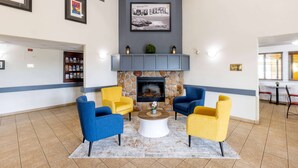 Un hall d’entrée agrémenté d’une cheminée en pierre, de fauteuils bleus et jaunes, d’une table basse et d’œuvres d’art encadrées qui ornent les murs.