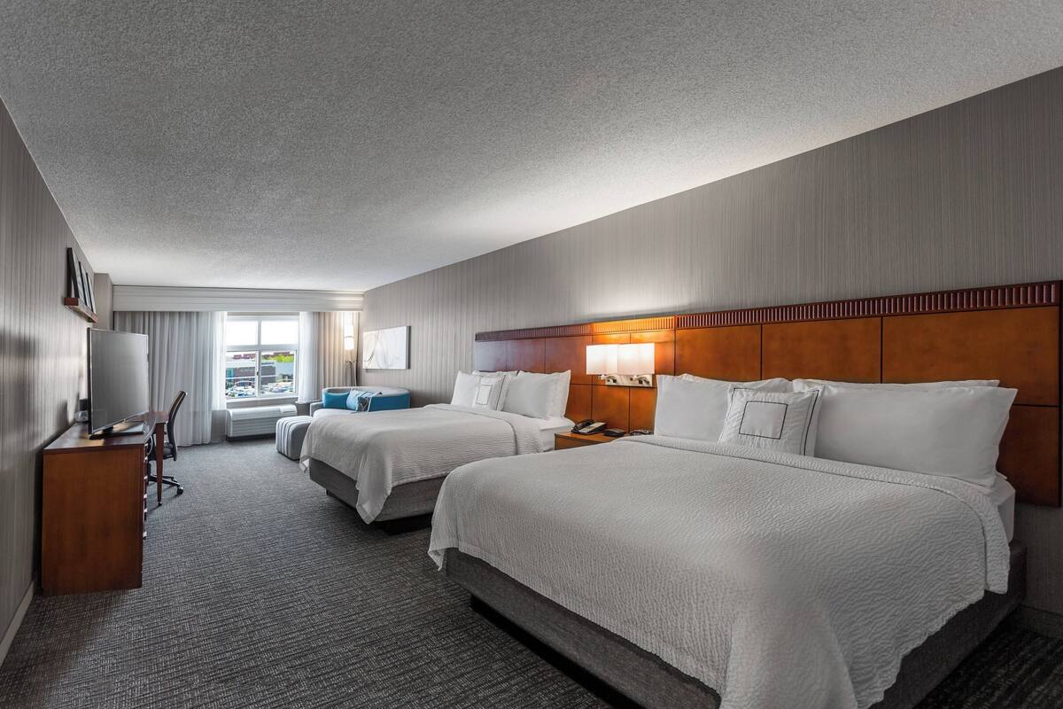 A hotel room with two beds, a desk, a chair, a TV, and a window with curtains.