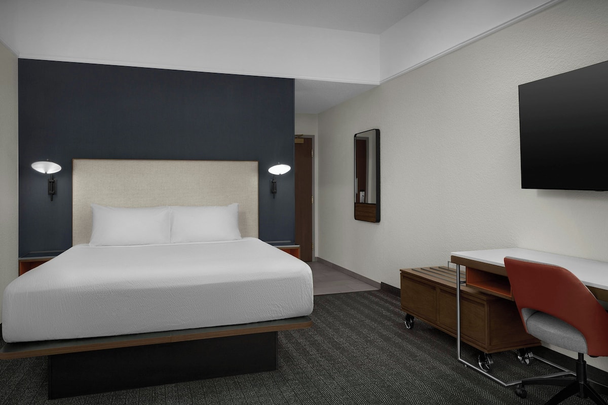 A hotel room with a bed, desk, chair, and a flat-screen TV mounted on the wall.