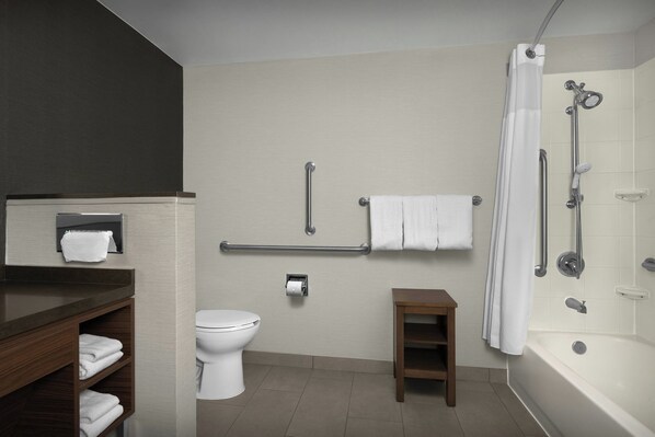 Un baño moderno con inodoro, ducha con puerta de vidrio, tocador con espejo y un pequeño taburete de madera.