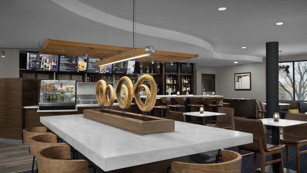 Un área de bar moderna con una isla central, detalles de madera y una pantalla de menú.