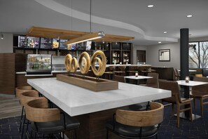 Un área de bar moderna con una isla central, detalles de madera y una pantalla de menú.