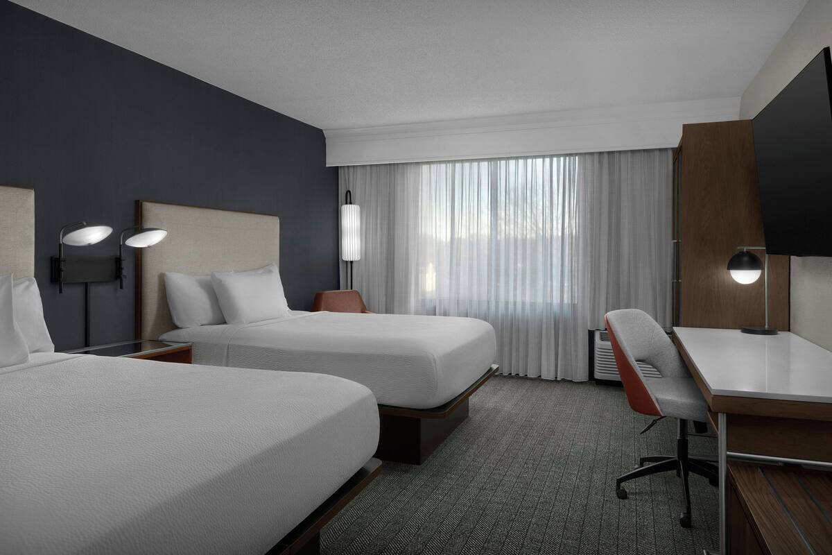 A hotel room with two beds, a desk, and a chair.