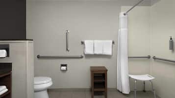 Un bagno con il water, maniglie di sostegno, un piccolo sgabello e una doccia con tenda.