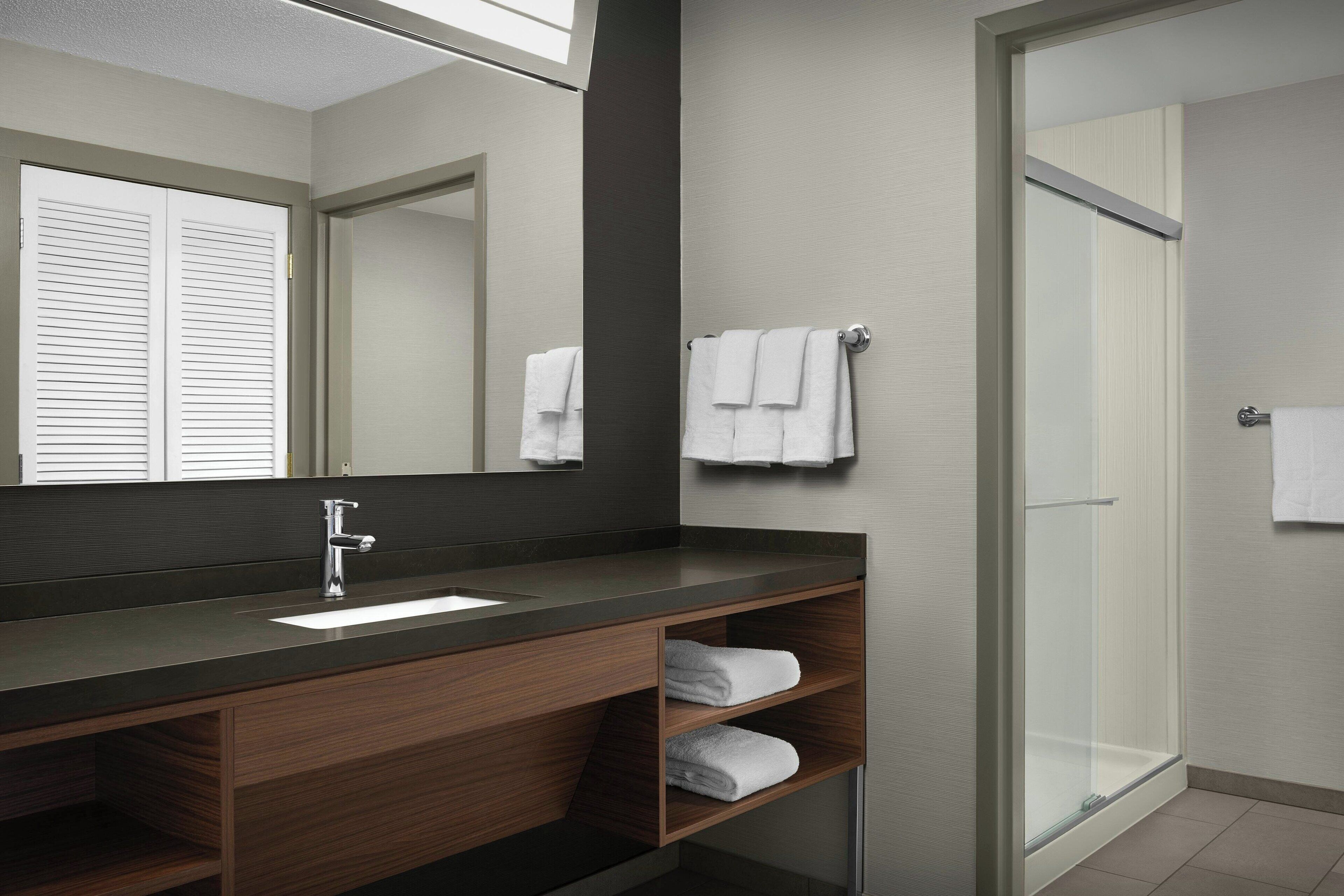A modern bathroom with a dark countertop, a mirror, a sink, and a glass shower enclosure.