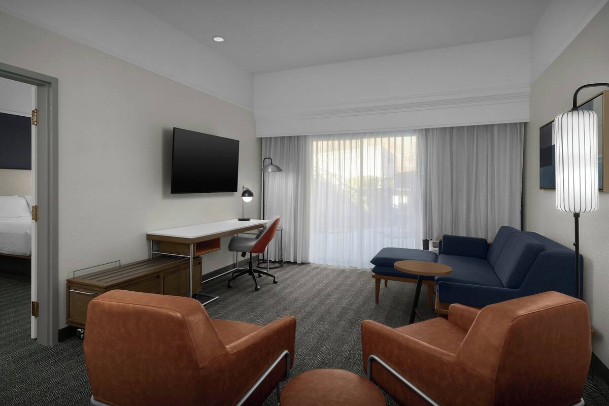 A hotel room with a bed, a desk, a TV, a sofa, and two armchairs.
