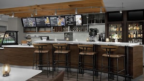 Un área de bar moderna con techo de madera, varias pantallas mostrando menús y una gran variedad de botellas y vasos en estanterías.