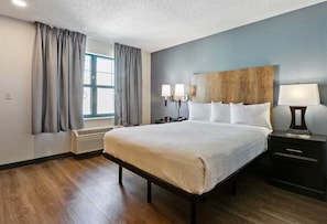 A hotel room with a large bed, a wooden headboard, a nightstand, a lamp, and a window with curtains.
