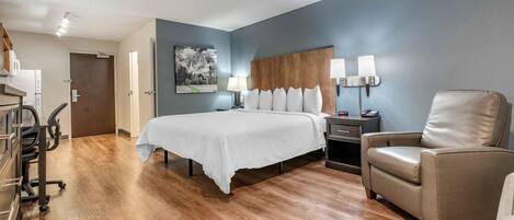 A hotel room with a bed, a desk, a chair, and a painting on the wall.