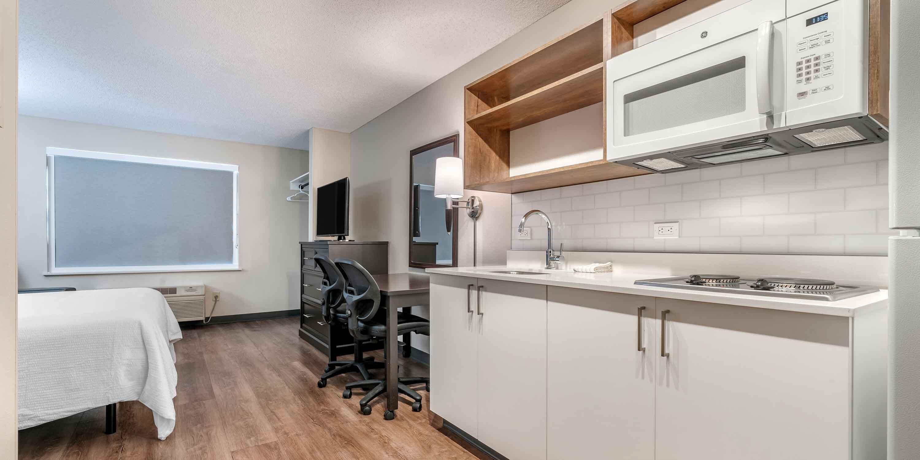 A compact kitchen with white cabinets, a microwave, a stove, and a sink. There is a small office area with a desk and chairs.