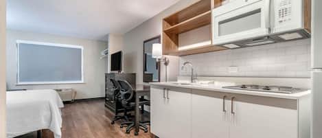 Una cocina compacta con armarios blancos, un microondas, una estufa y un lavamanos. Cuenta con una pequeña zona de trabajo con un escritorio y sillas.
