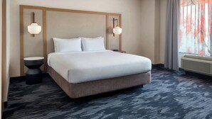 A hotel room with a large bed, two bedside tables, a wall-mounted light fixture, and a window with curtains. - Fairfield Inn & Suites by Marriott Woodbridge (Avenel)